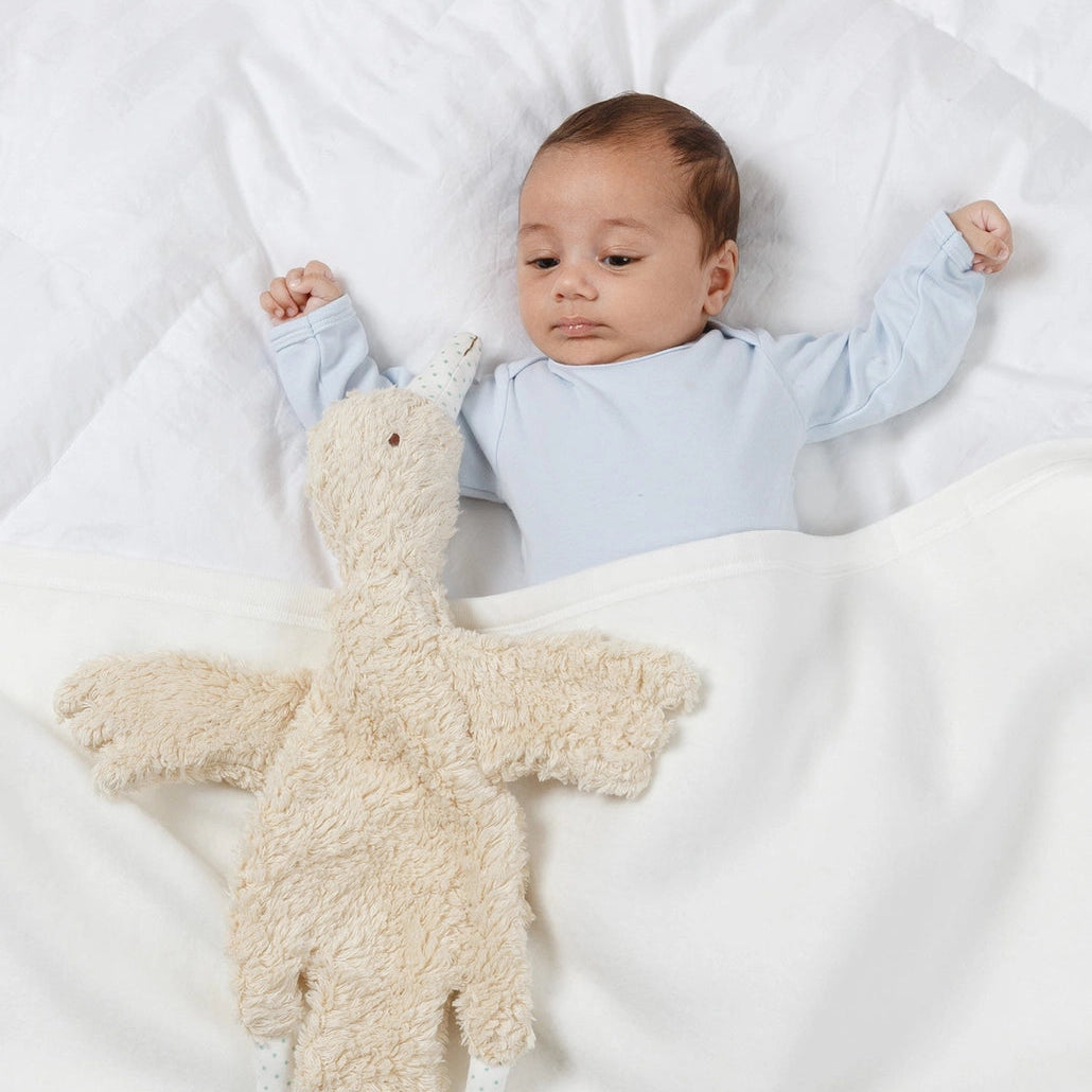 Baby lying on a white blanket with a plush toy next to them